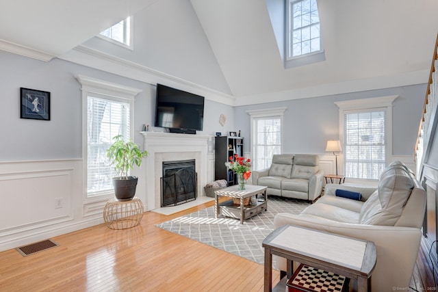 living room featuring a fireplace with flush hearth, a wealth of natural light, a wainscoted wall, and visible vents