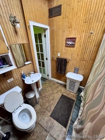 bathroom with toilet and wood walls