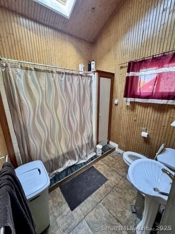 bathroom with wood walls, toilet, vaulted ceiling with skylight, and curtained shower