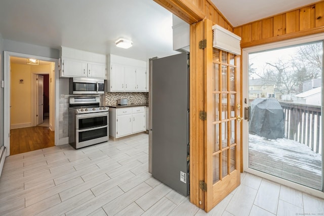 kitchen featuring white cabinetry, appliances with stainless steel finishes, light wood-type flooring, tasteful backsplash, and dark countertops