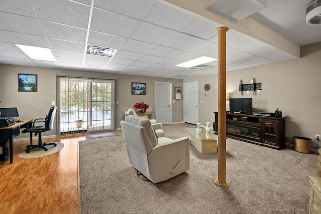 living area featuring a paneled ceiling, visible vents, baseboards, and wood finished floors