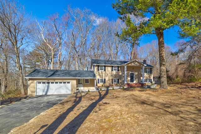 view of front of house with an attached garage, a chimney, and aphalt driveway