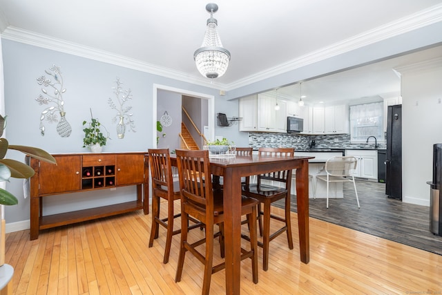 dining room with ornamental molding, a notable chandelier, stairway, and light wood finished floors