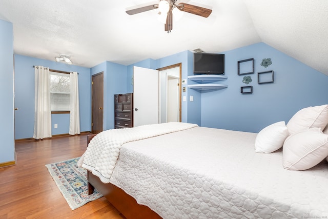 bedroom with baseboards, a ceiling fan, wood finished floors, vaulted ceiling, and a textured ceiling