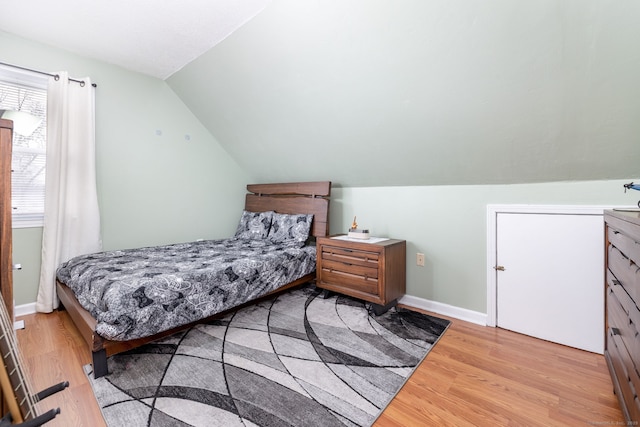 bedroom with vaulted ceiling, wood finished floors, and baseboards