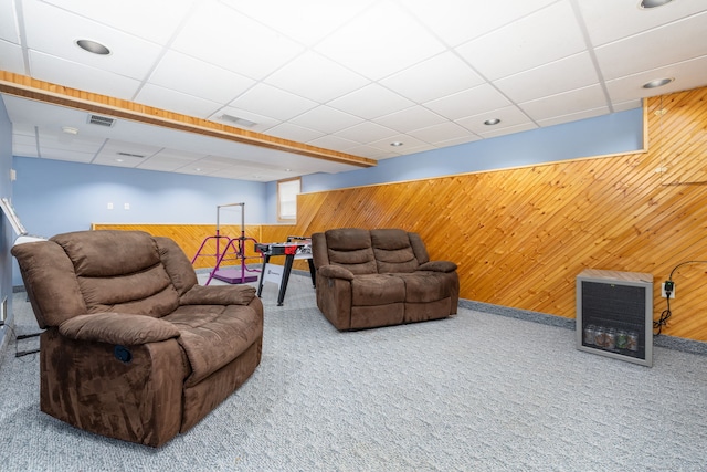 carpeted living area featuring a paneled ceiling, wainscoting, visible vents, and wooden walls