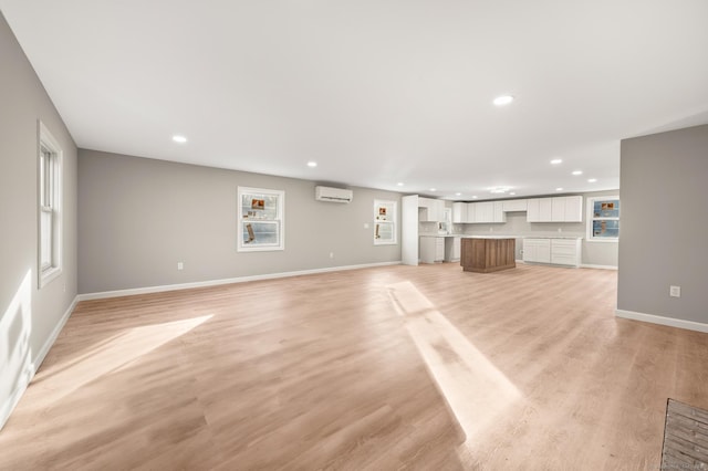 unfurnished living room featuring light wood-style floors, recessed lighting, an AC wall unit, and baseboards