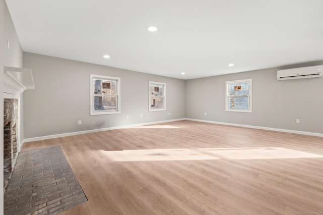 unfurnished living room featuring light wood-type flooring, a wall unit AC, a fireplace, and baseboards