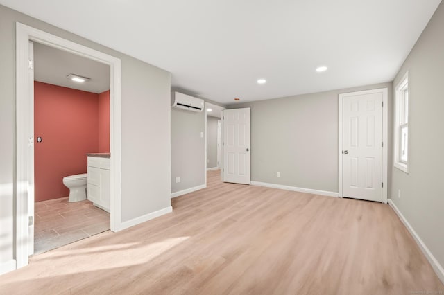 unfurnished bedroom featuring a barn door, baseboards, light wood-style floors, a wall mounted AC, and ensuite bath