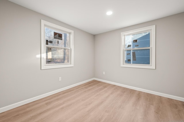 spare room with baseboards, light wood-type flooring, and a healthy amount of sunlight