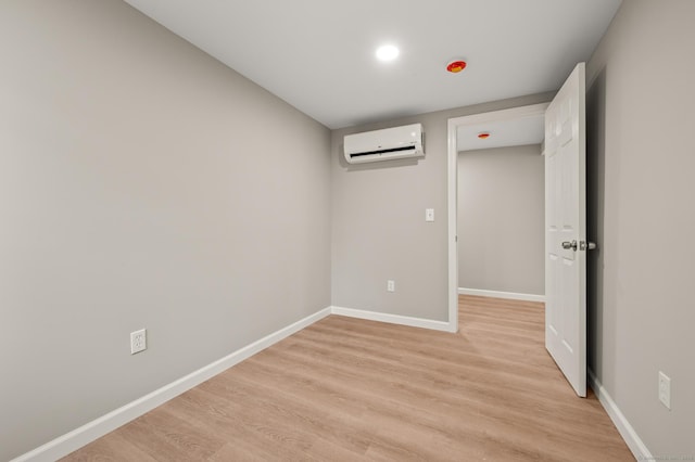 spare room featuring baseboards, a wall mounted air conditioner, and light wood finished floors