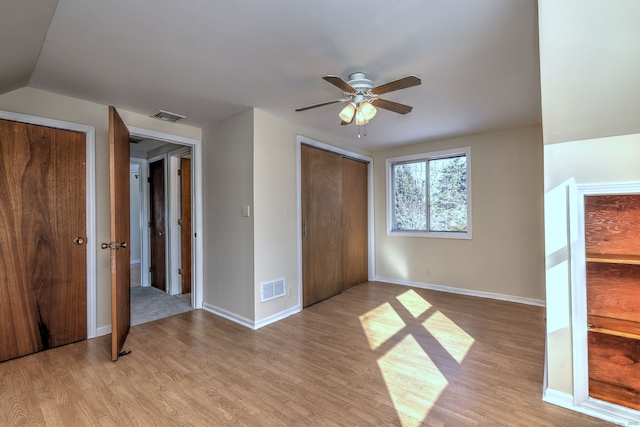 unfurnished bedroom featuring light hardwood / wood-style floors, lofted ceiling, ceiling fan, and two closets