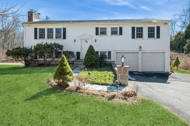 split foyer home featuring a garage, aphalt driveway, a chimney, and a front lawn