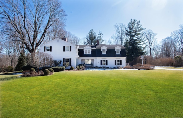 colonial inspired home featuring a front yard, a chimney, and a gambrel roof