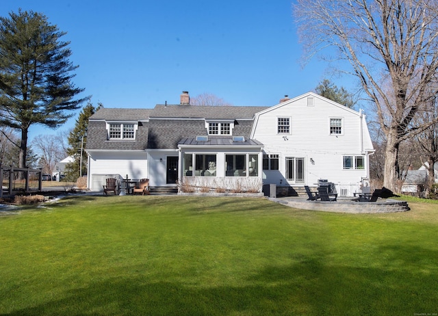 back of property with a patio, a chimney, a shingled roof, a lawn, and a gambrel roof