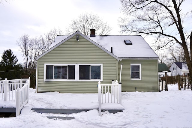 snow covered house with fence and a chimney