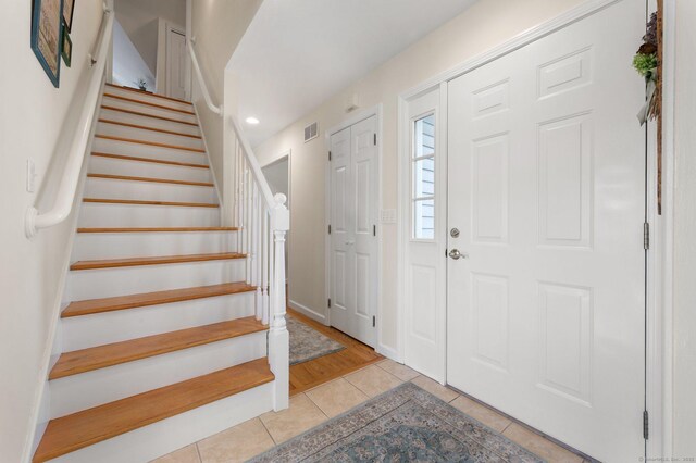 entryway featuring light tile patterned flooring, visible vents, baseboards, and stairs