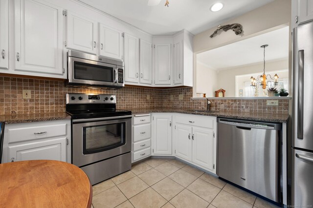 kitchen featuring stainless steel appliances, a sink, white cabinetry, backsplash, and decorative light fixtures