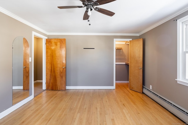 unfurnished bedroom featuring ornamental molding, light hardwood / wood-style floors, a walk in closet, and a baseboard heating unit