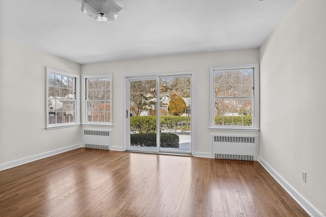 unfurnished room with radiator, a wealth of natural light, and hardwood / wood-style flooring