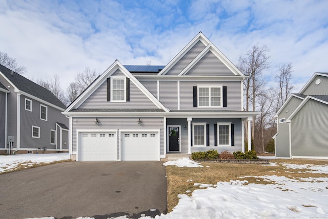 view of front of home featuring an attached garage, covered porch, aphalt driveway, and solar panels