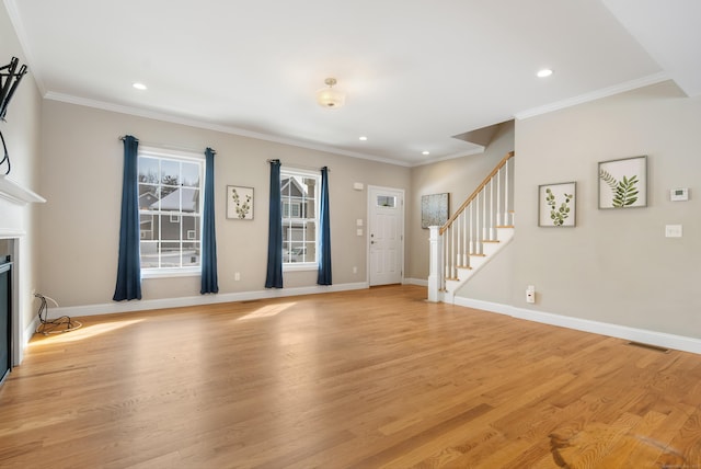 unfurnished living room with crown molding, light wood-style flooring, a glass covered fireplace, baseboards, and stairs