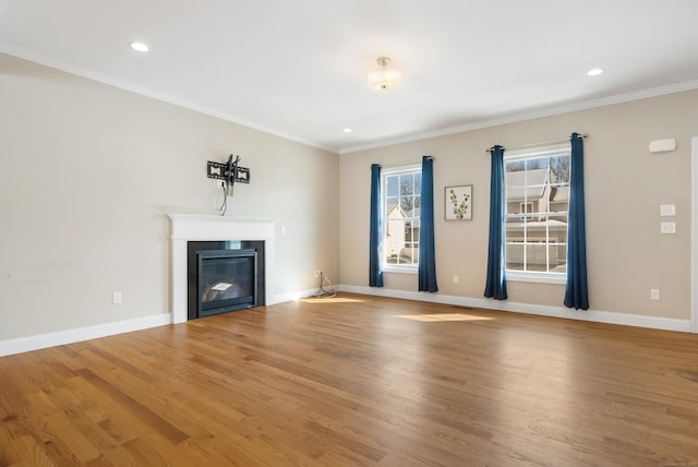 unfurnished living room featuring crown molding, baseboards, wood finished floors, and a glass covered fireplace