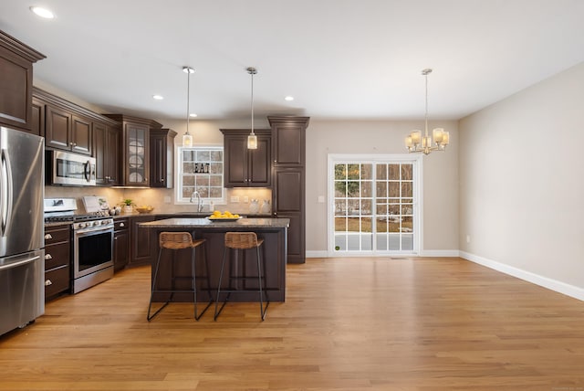 kitchen with light wood finished floors, appliances with stainless steel finishes, a breakfast bar, and dark brown cabinets