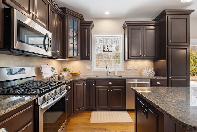 kitchen with dark stone counters, appliances with stainless steel finishes, a sink, and dark brown cabinetry