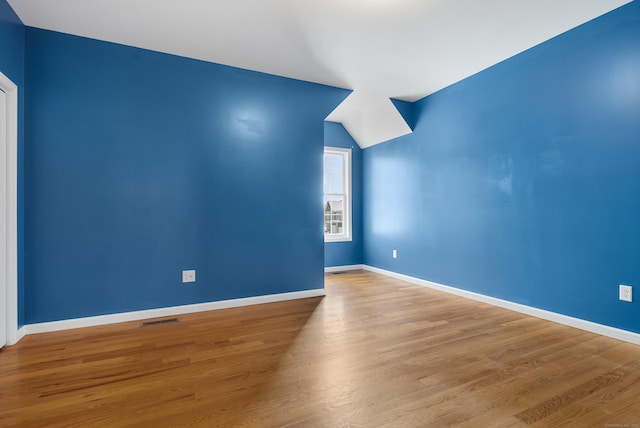 empty room with lofted ceiling, wood finished floors, visible vents, and baseboards