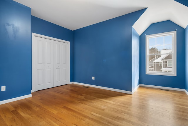 unfurnished bedroom with visible vents, baseboards, vaulted ceiling, light wood-style floors, and a closet