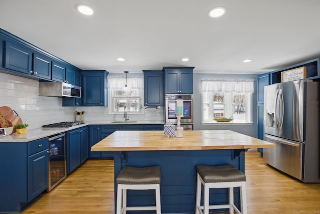 kitchen featuring beverage cooler, butcher block countertops, appliances with stainless steel finishes, a breakfast bar, and blue cabinets