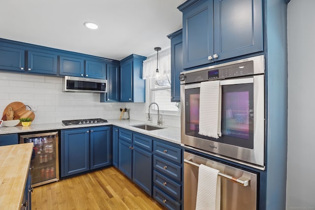 kitchen with decorative light fixtures, stainless steel appliances, wooden counters, a sink, and beverage cooler