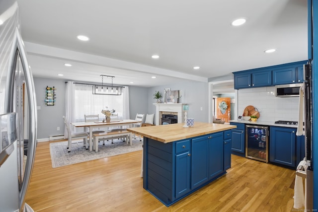 kitchen with a center island, blue cabinetry, stainless steel appliances, wooden counters, and beverage cooler