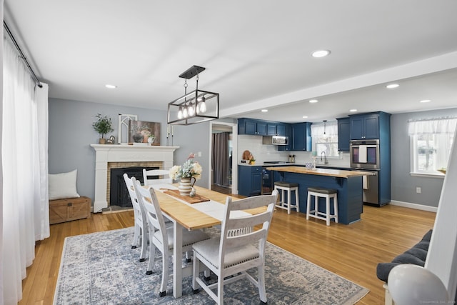 dining room with baseboards, recessed lighting, a brick fireplace, and light wood-style floors