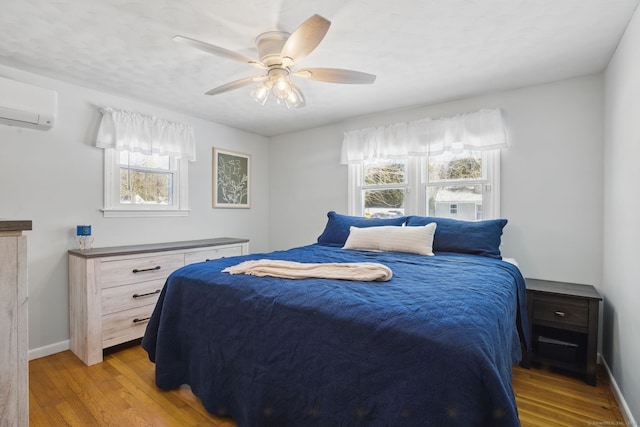 bedroom featuring light wood-style flooring, baseboards, ceiling fan, and a wall mounted AC