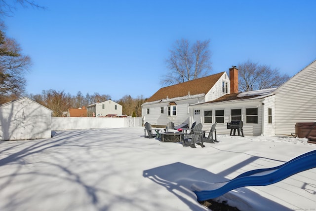 snow covered back of property with a chimney, a fire pit, and fence