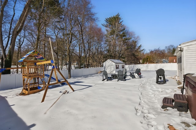 yard covered in snow featuring an outbuilding, a fenced backyard, a playground, and a storage unit