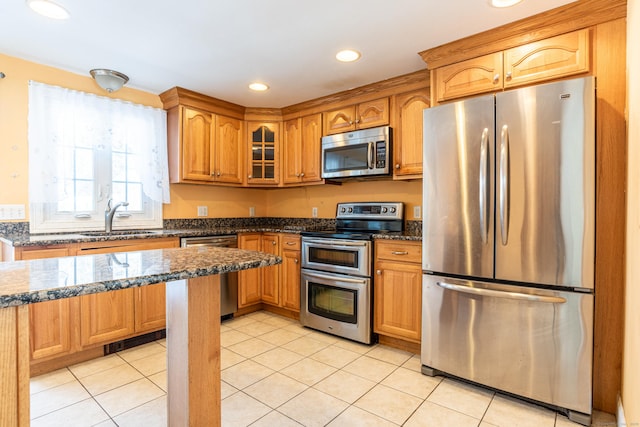 kitchen with dark stone counters, appliances with stainless steel finishes, a sink, and glass insert cabinets