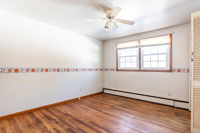 spare room with a baseboard heating unit, ceiling fan, dark wood-type flooring, and baseboards