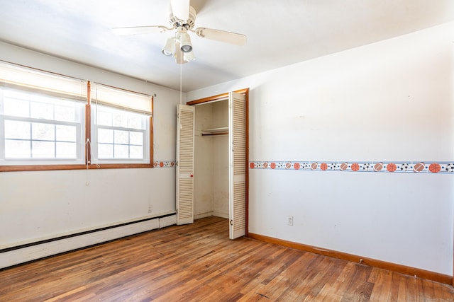 unfurnished bedroom featuring a baseboard radiator, a closet, baseboards, and wood finished floors