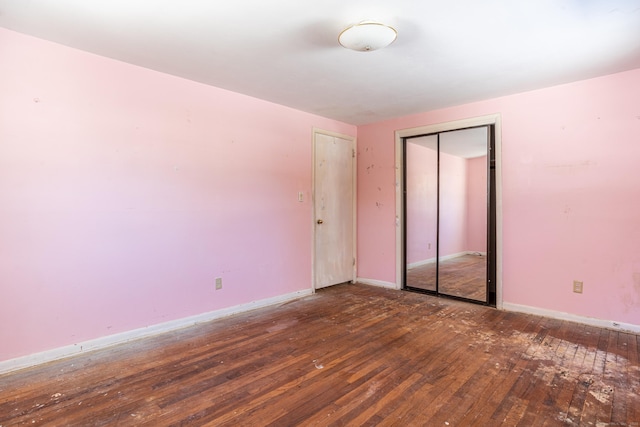 unfurnished bedroom with dark wood-style floors, a closet, and baseboards