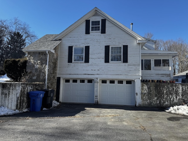 view of side of home featuring stone siding, driveway, and an attached garage