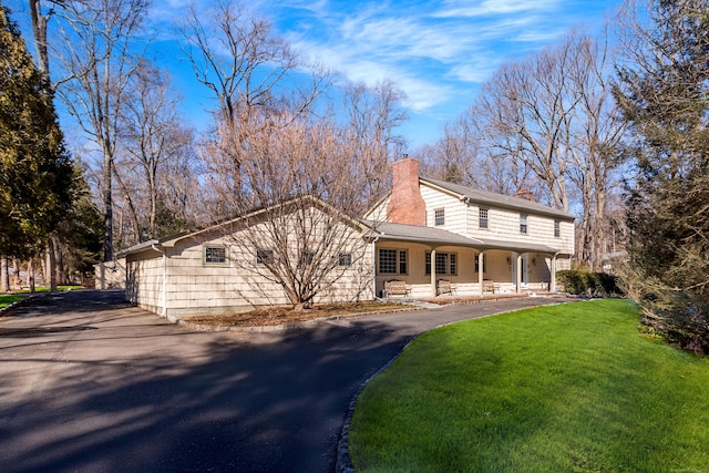 view of front of home with driveway, a chimney, a front lawn, and a porch