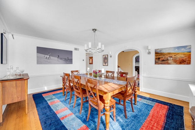 dining room featuring arched walkways, wood finished floors, visible vents, ornamental molding, and an inviting chandelier