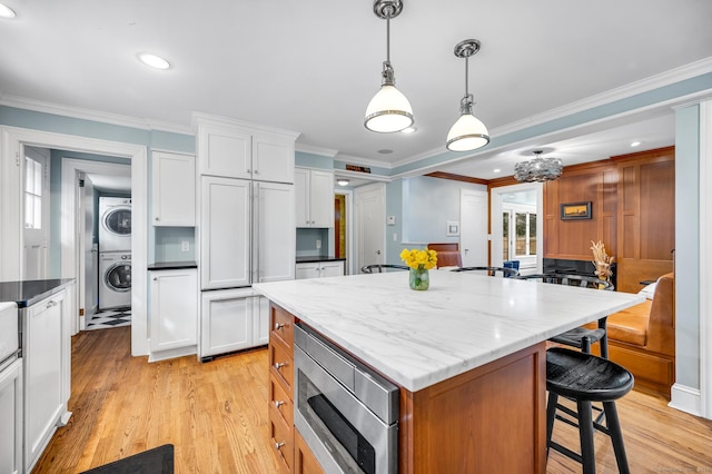 kitchen featuring white cabinets, a kitchen island, built in appliances, stacked washing maching and dryer, and a kitchen bar