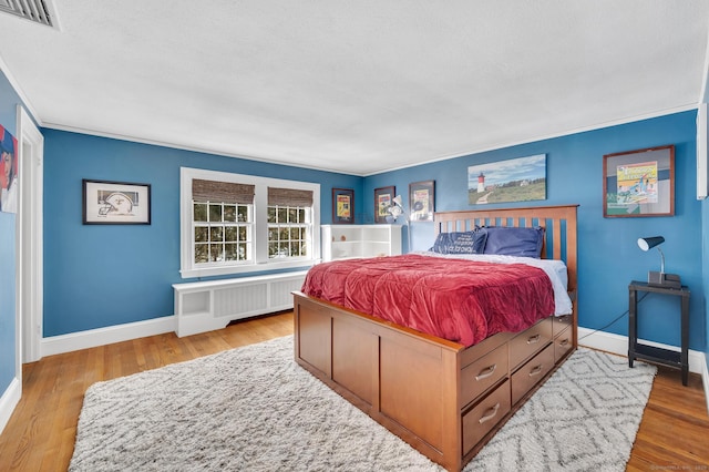 bedroom featuring baseboards, visible vents, radiator heating unit, and wood finished floors