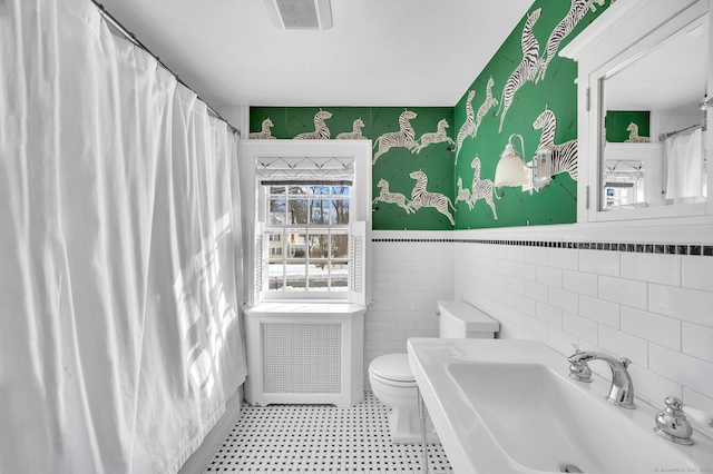 full bath with a wainscoted wall, tile walls, visible vents, toilet, and a sink