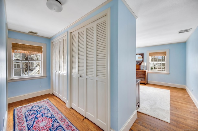 hallway with light wood-style floors, baseboards, and visible vents