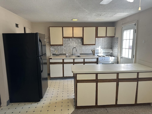 kitchen with freestanding refrigerator, gas range gas stove, light countertops, light floors, and a sink